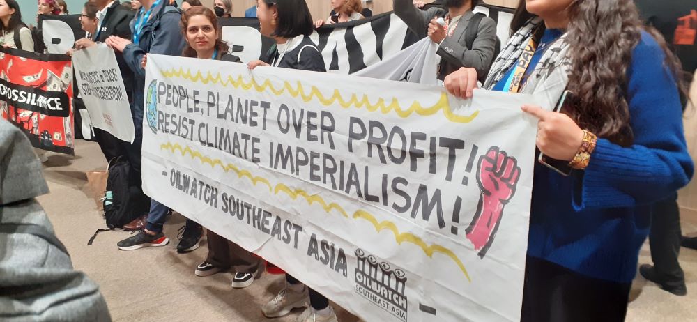 protesters holding a sign saying 'people, planet over profit! resist climate imperialism'