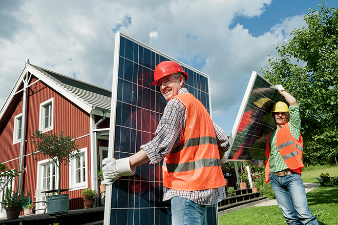 To arbeidere bærer på solpanel foran en enebolig.