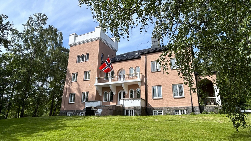Tre etasjers flott mursteinbygning omkranset av gressplen og trær