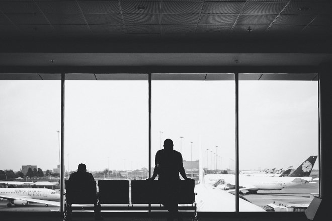 Two passengers looking at a plane through a window at an airport