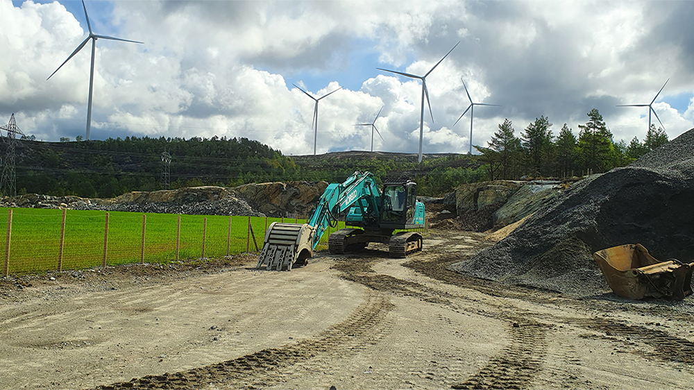 Anleggsområde med en gravemaskin og i bakgrunnen vindturbiner i snaufjlellsområde