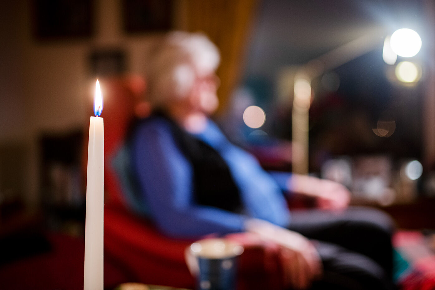 Person siter i en stol i bakgrunnen, foran er et stearinlys