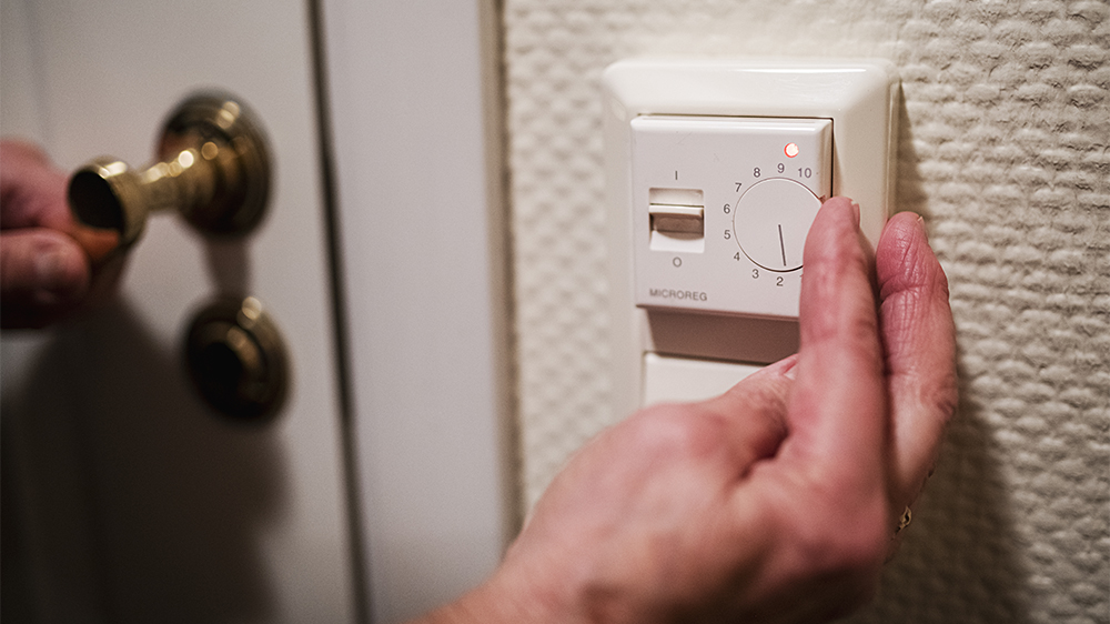  Close-up of hand turning on a wall thermostat.